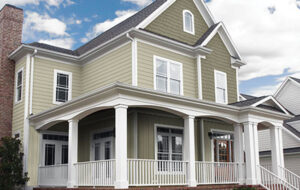 A large home with a wrap around porch has green vinyl house siding.